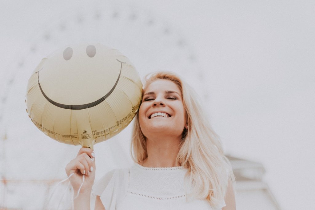 Woman smiling while holding a smiley face balloon