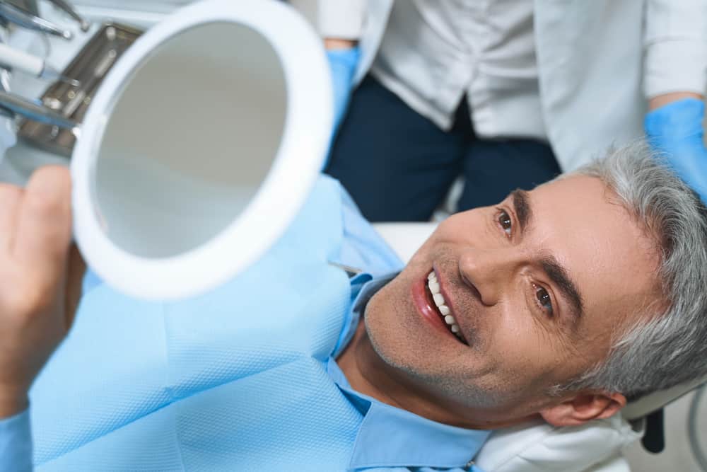 Joyful male is lying in chair and looking into mirror while being delighted with dentist work